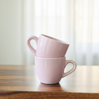 Two pink mugs stacked on a wooden table with a blurred indoor background