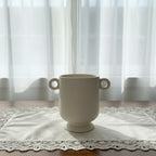 White ceramic vase with handles on a wooden surface and light background